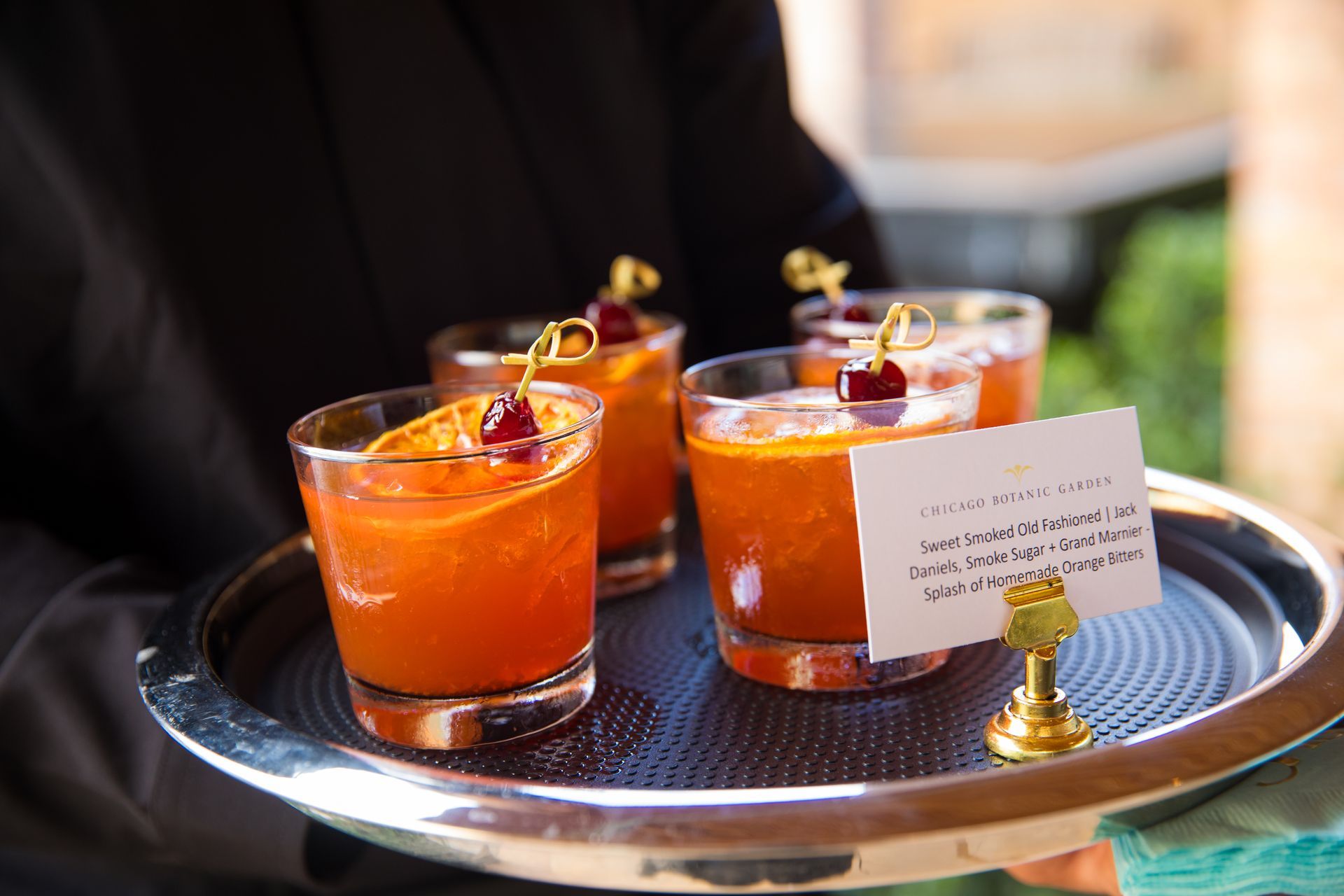 A waiter is holding a tray of cocktails on a stick.