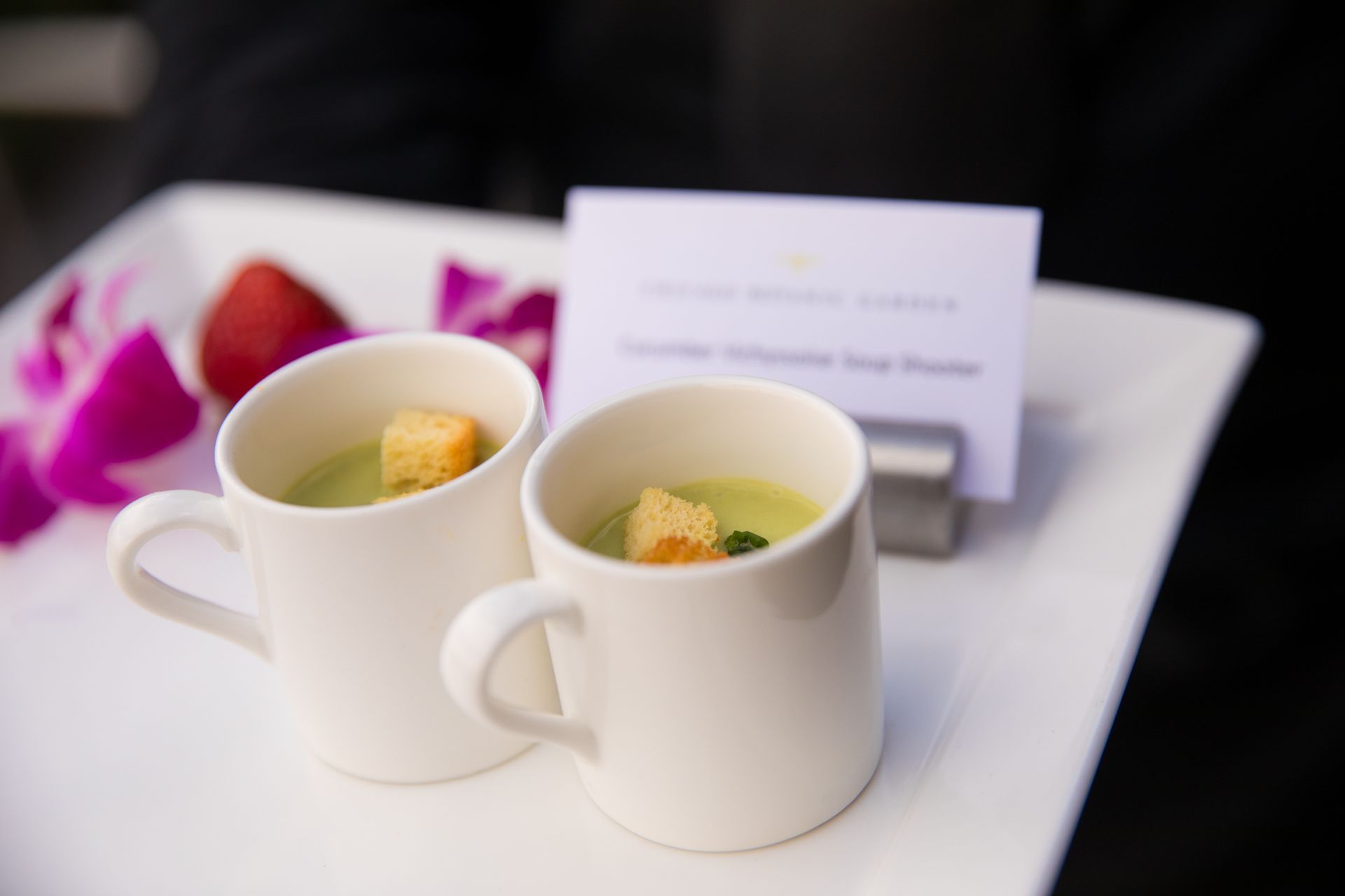 Two cups of soup with croutons on a white plate.