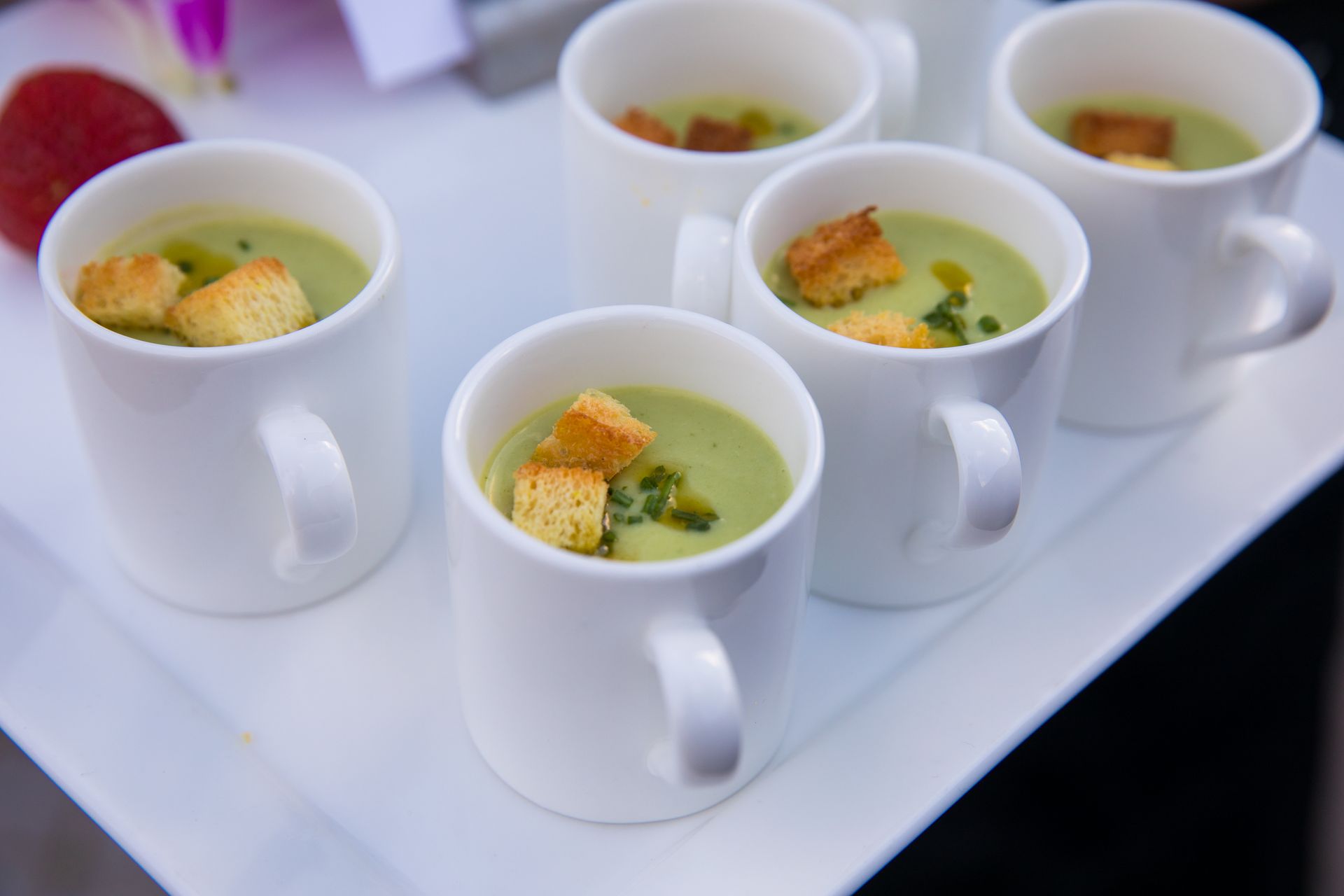 A tray of cups of soup with croutons on top.