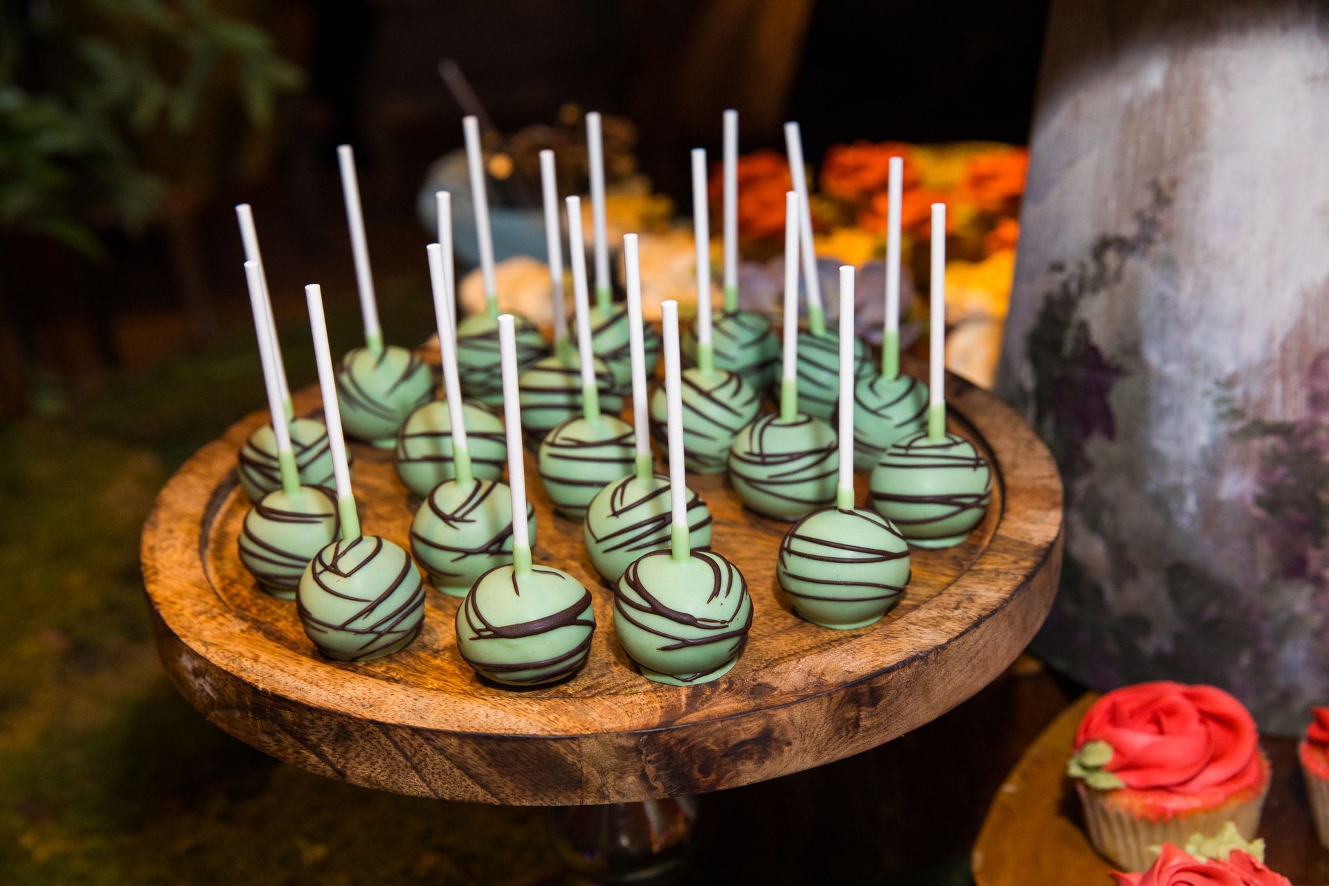 A wooden plate topped with green cake pops and cupcakes.