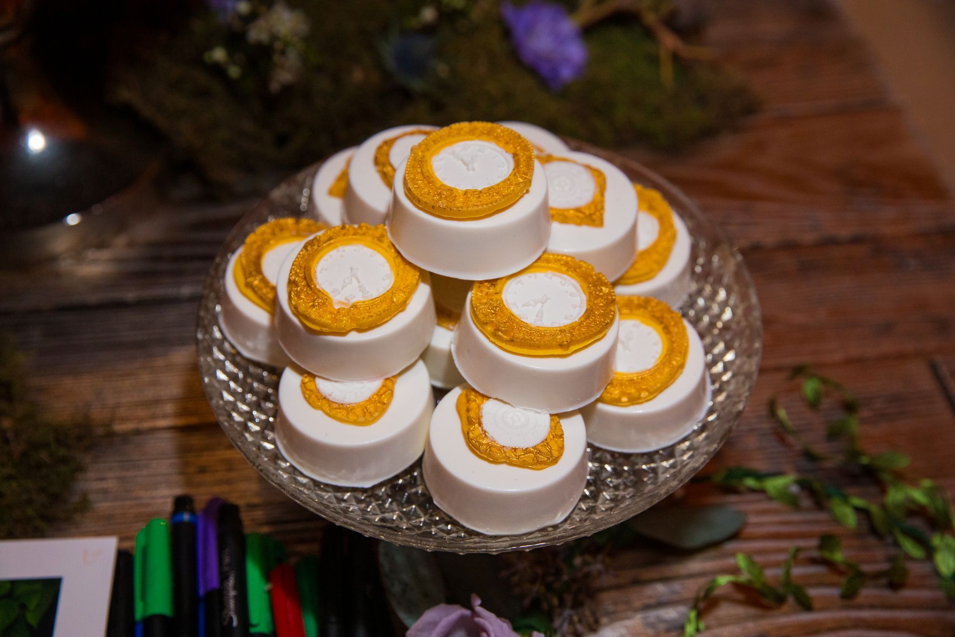 A glass plate topped with white and gold cookies on a wooden table.