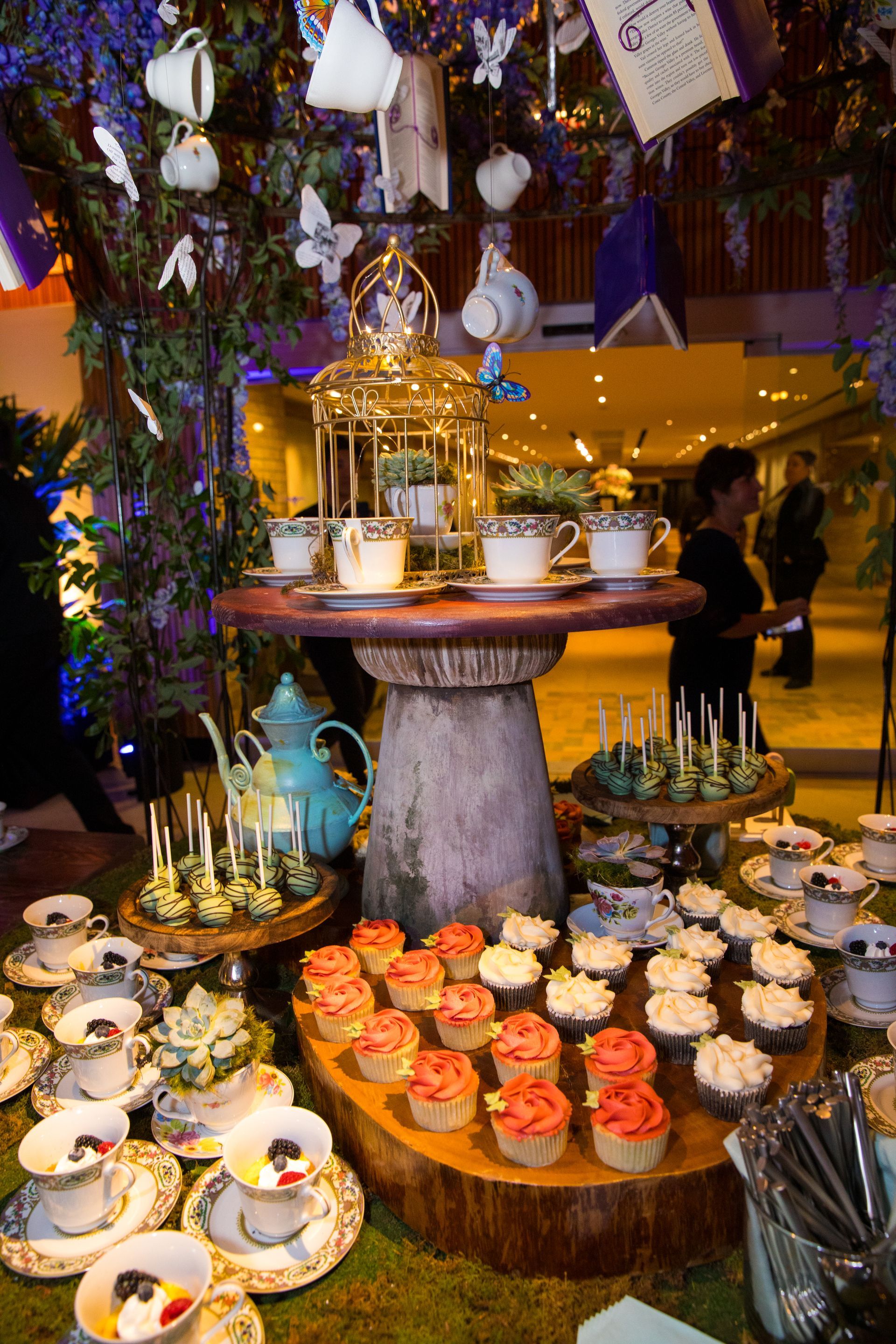 A table topped with cupcakes , cups , saucers and a bird cage.