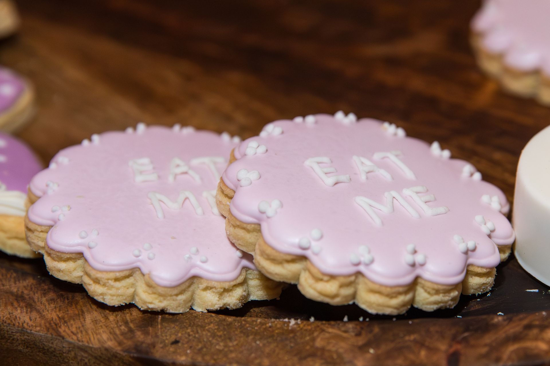 Two purple cookies that say eat me are on a wooden table.