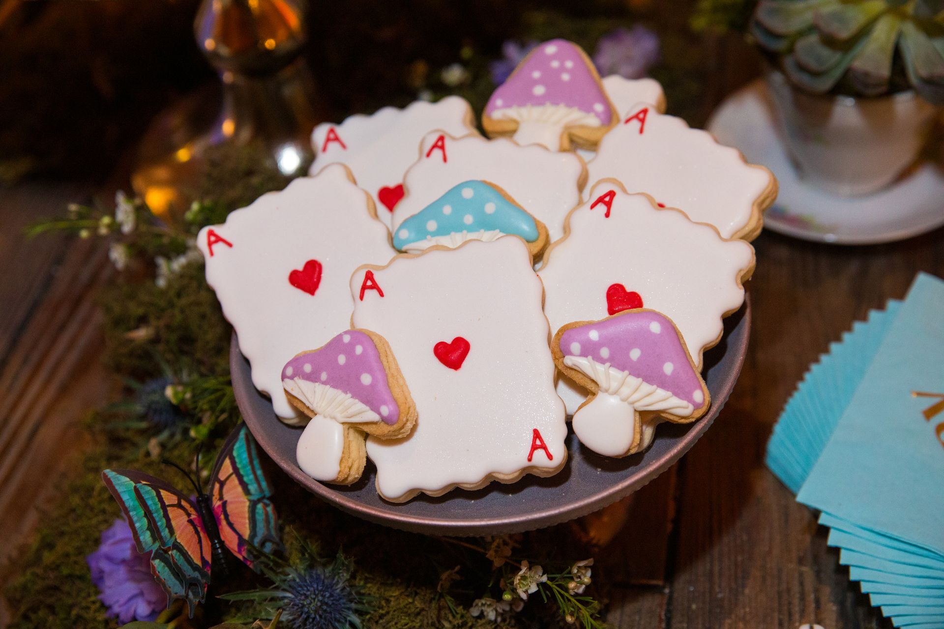 A plate of cookies decorated to look like playing cards and mushrooms on a table.