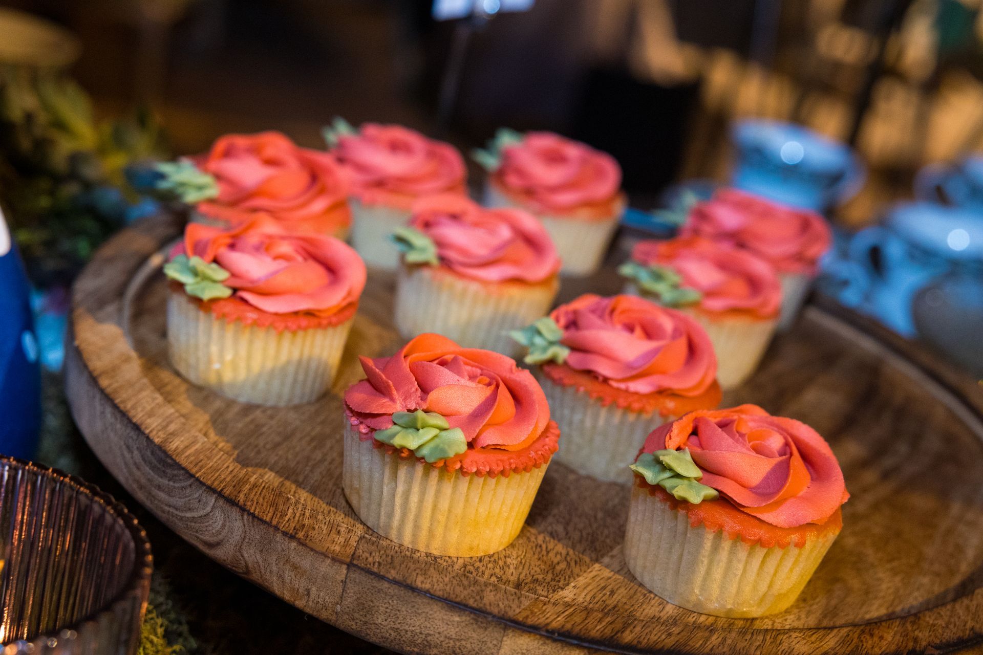 A wooden plate topped with cupcakes decorated with pink frosting and flowers.
