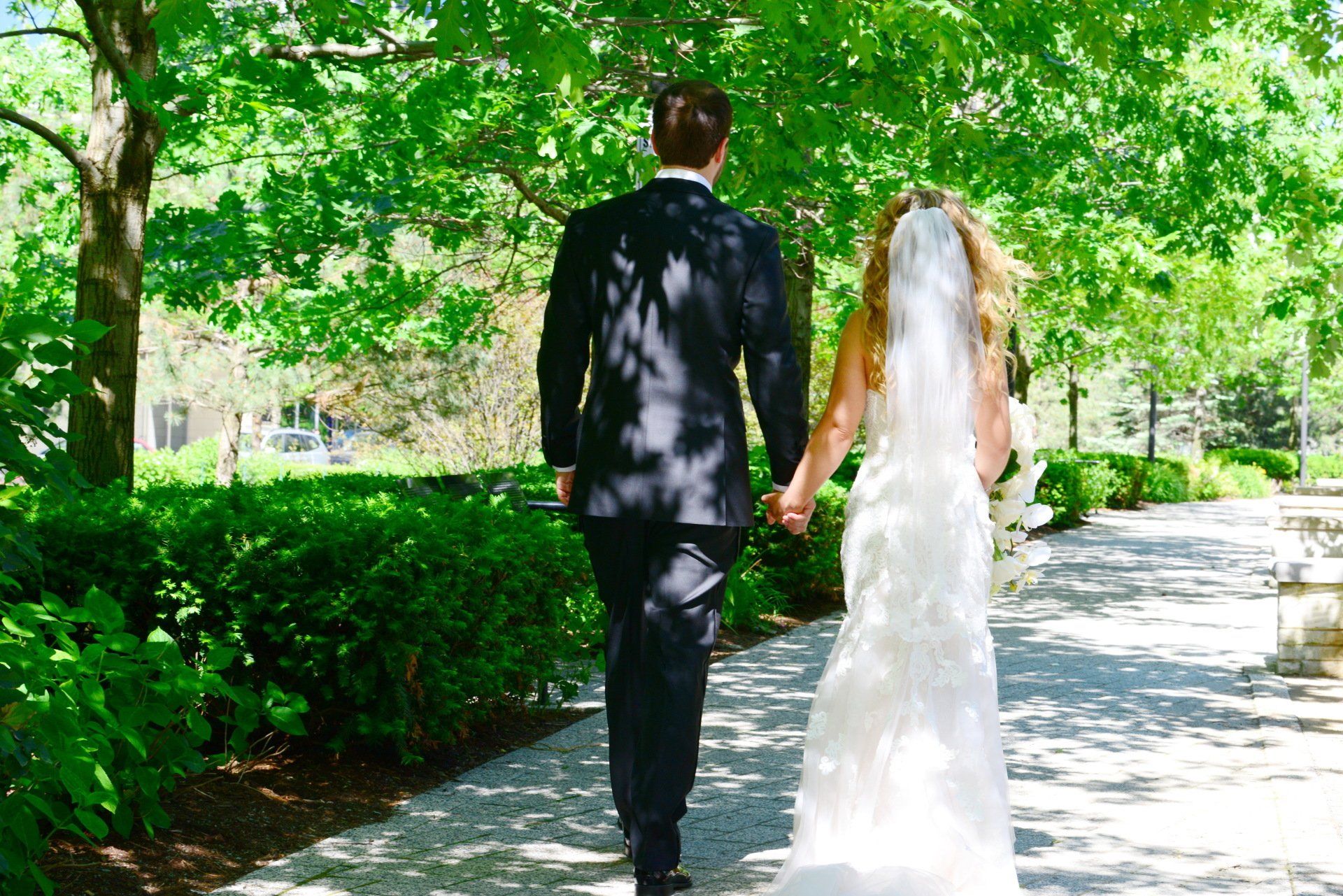 A bride and groom are walking down a path holding hands.