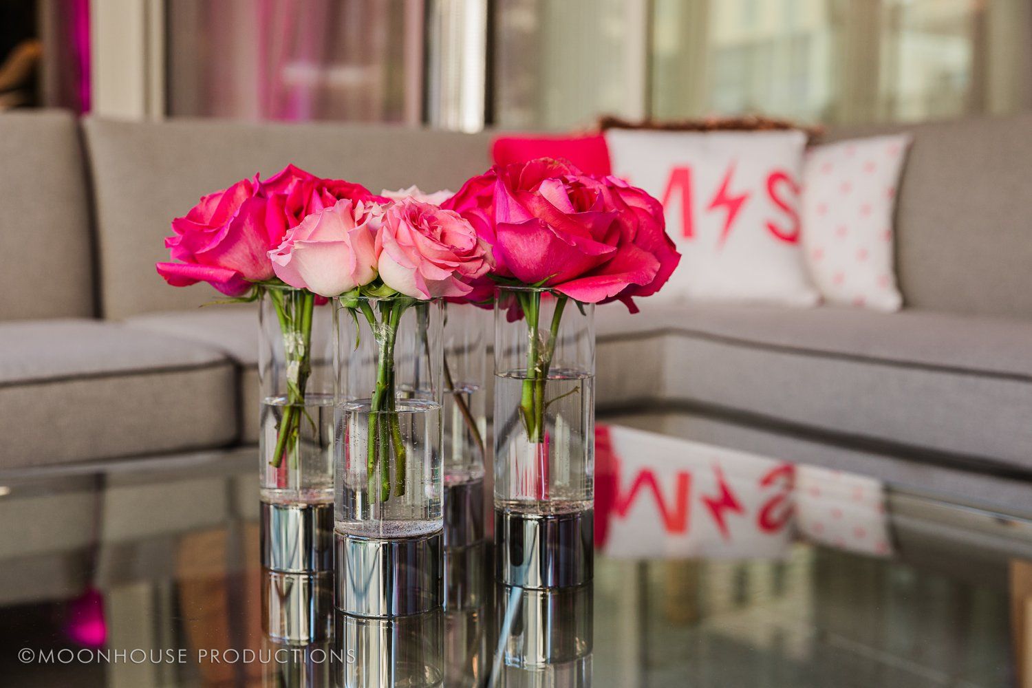 A vase of pink roses sits on a glass table next to a couch