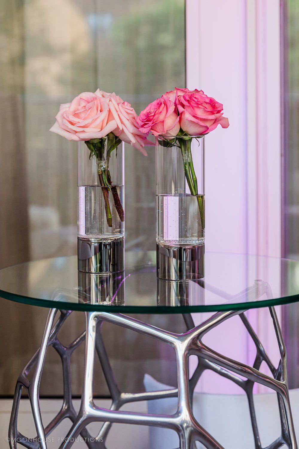 Two vases filled with pink roses are on a glass table.