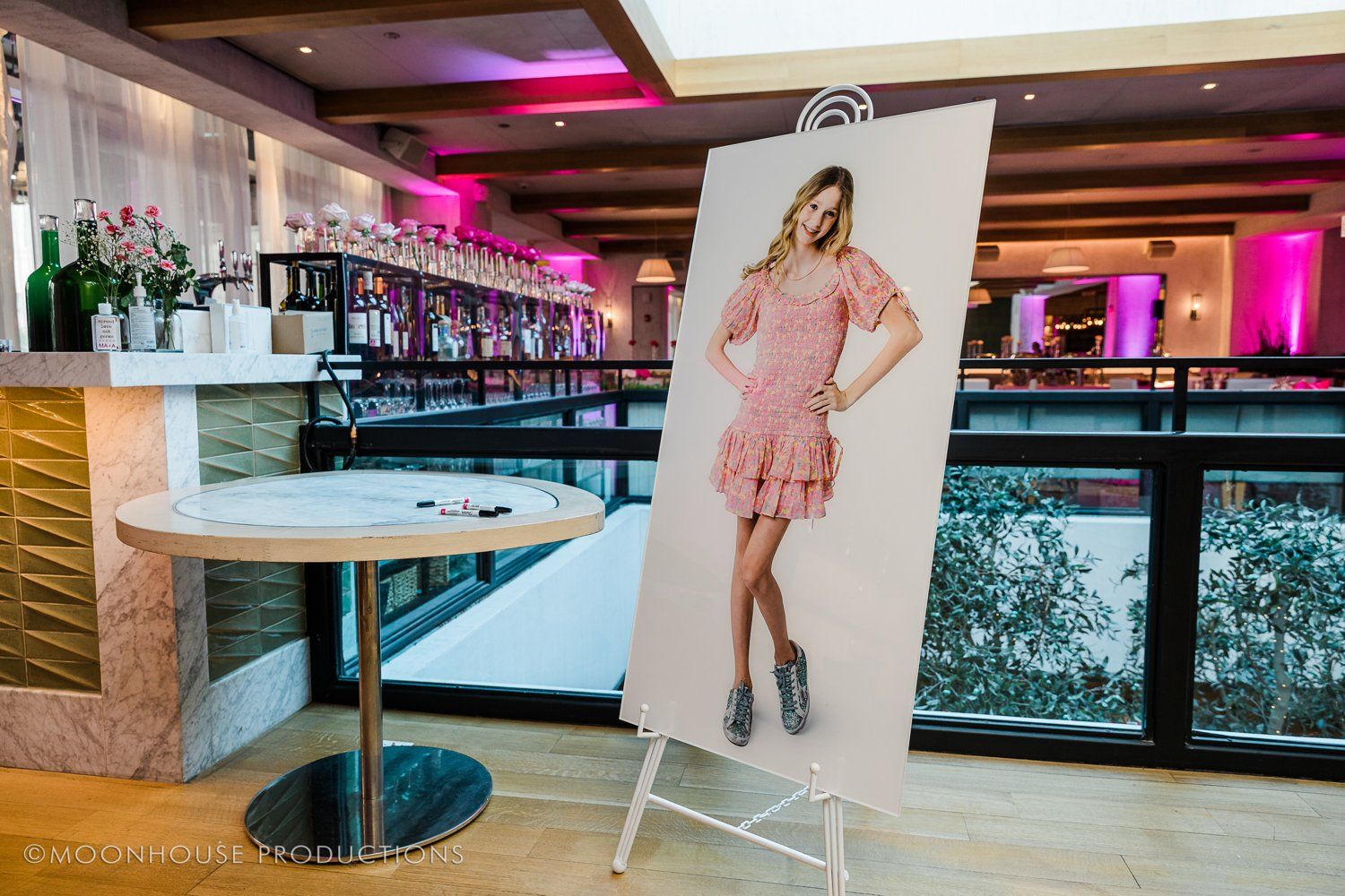 A large picture of a woman in a pink dress is on an easel in a room.