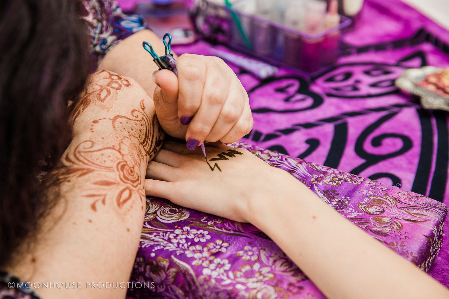 A woman is getting a henna tattoo on her hand.