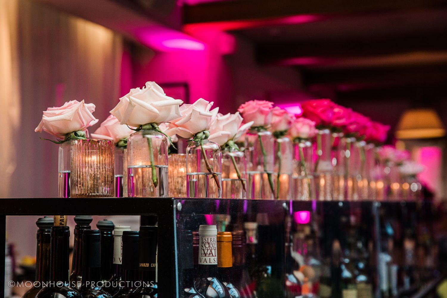 A row of vases filled with flowers and candles on a bar.