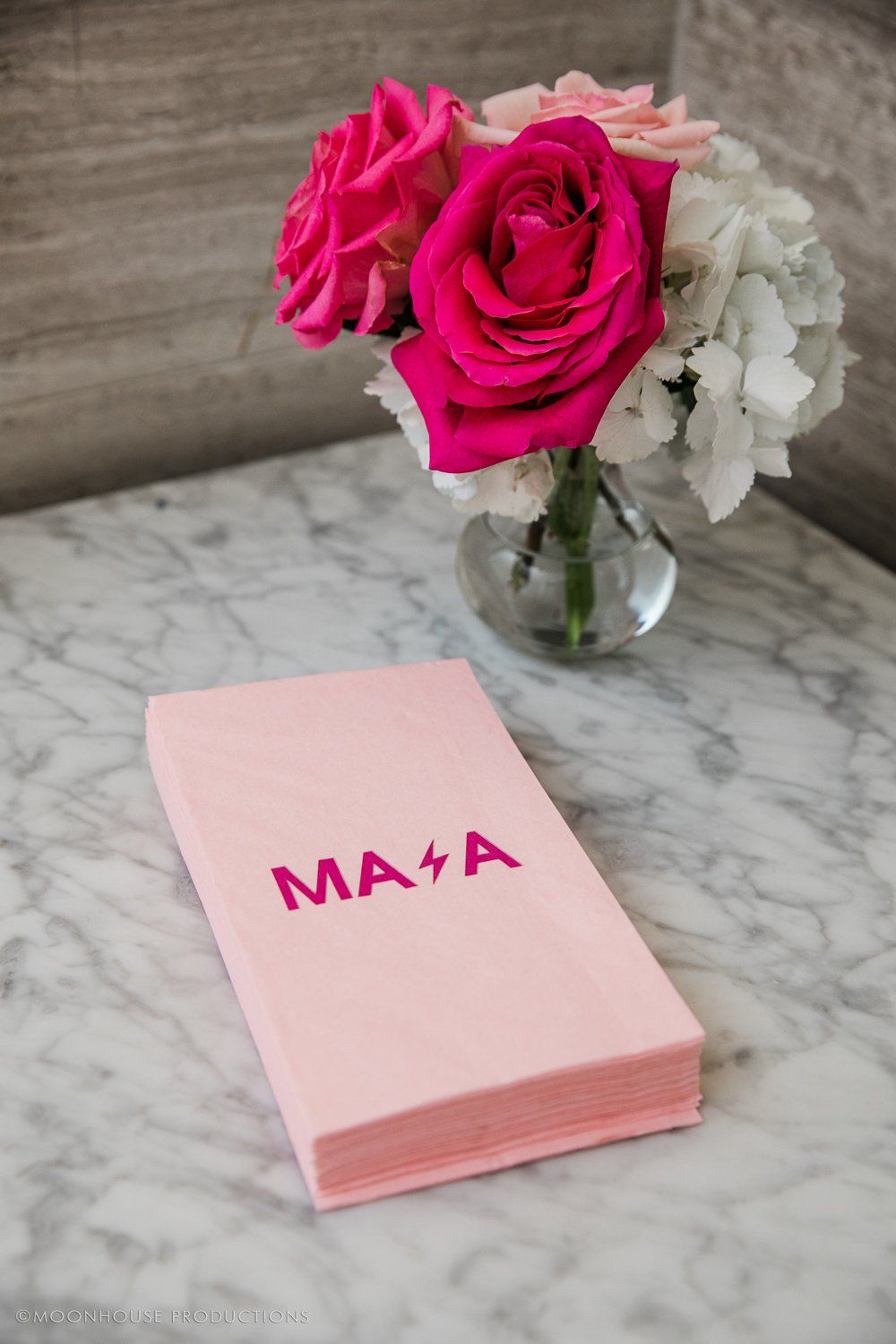 A pink napkin is sitting on a table next to a vase of pink roses.