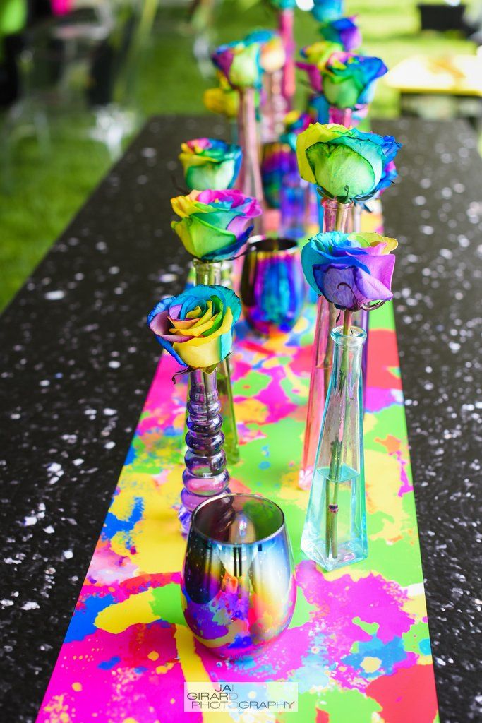 A table with a colorful table runner and vases of flowers on it.