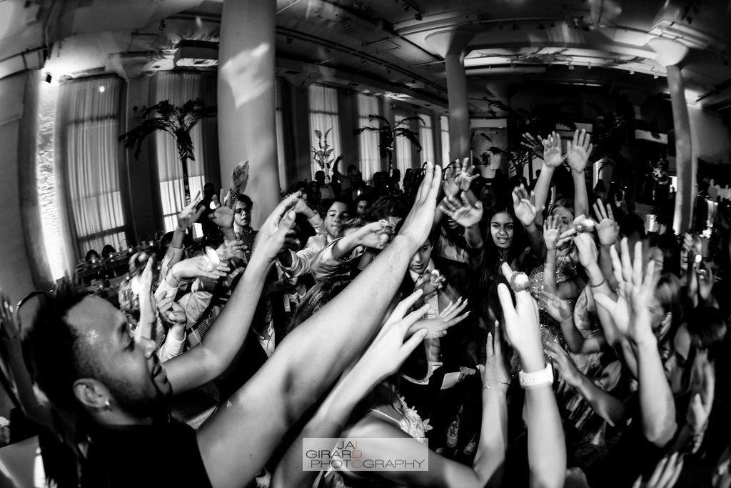 A black and white photo of a crowd of people raising their hands in the air.