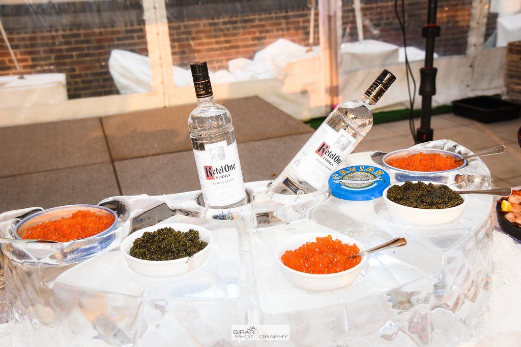 A table with a bottle of vodka and bowls of caviar on it.