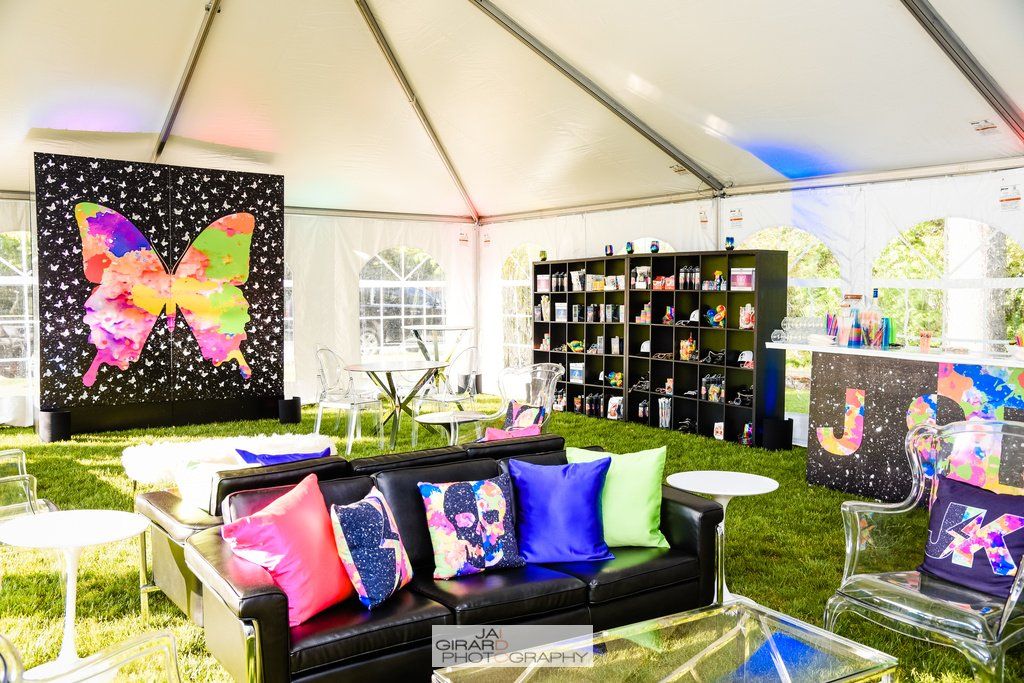 A tent with a couch , chairs , tables and a neon butterfly on the wall.