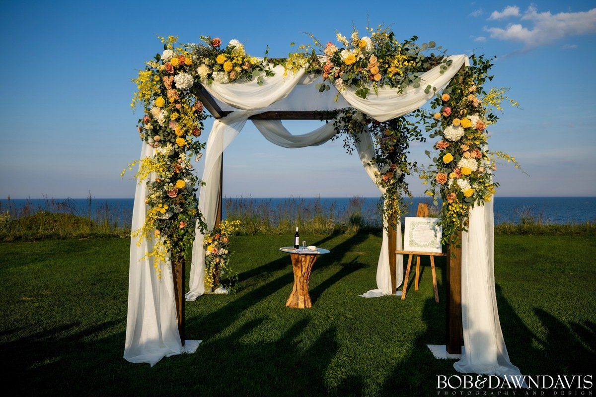 A wedding ceremony is taking place under a gazebo decorated with flowers.