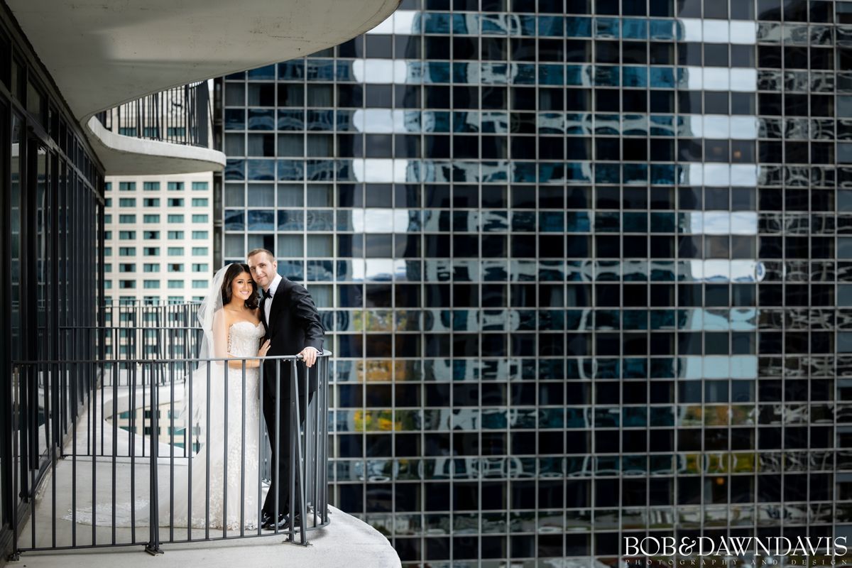 A bride and groom are posing for a picture on a balcony in front of a building.