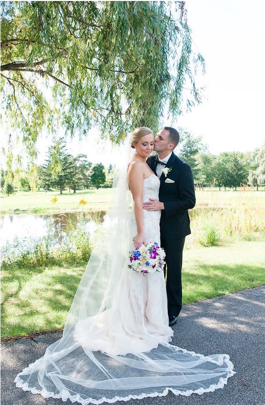 A bride and groom are kissing under a tree on their wedding day.