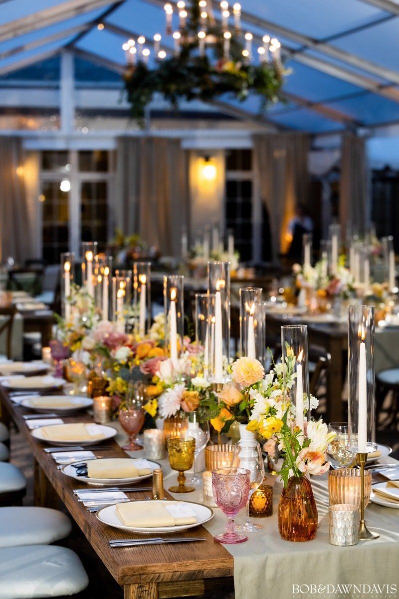 A long wooden table with plates , candles , and flowers on it.