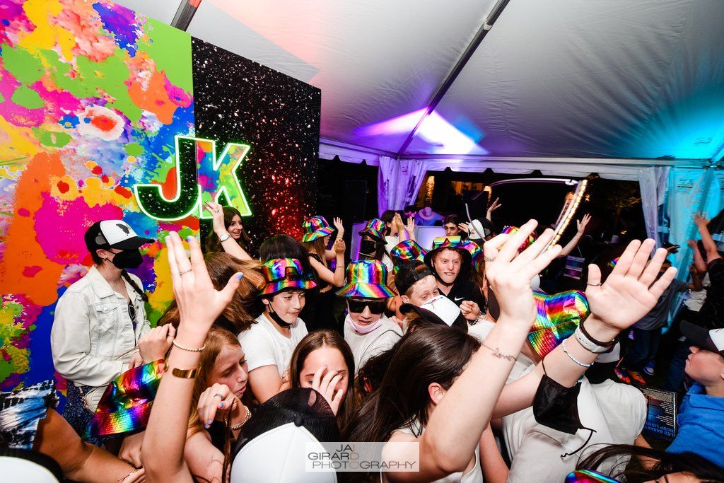 A crowd of people are dancing at a party with their hands in the air.