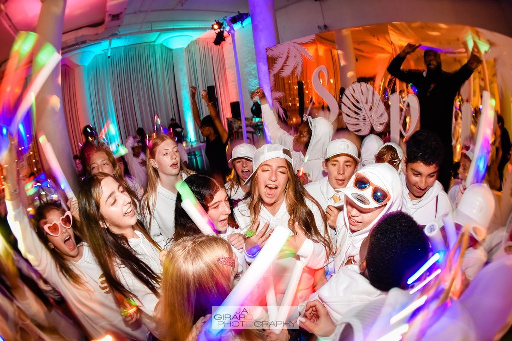 A group of people are dancing at a party with glow in the dark sticks.