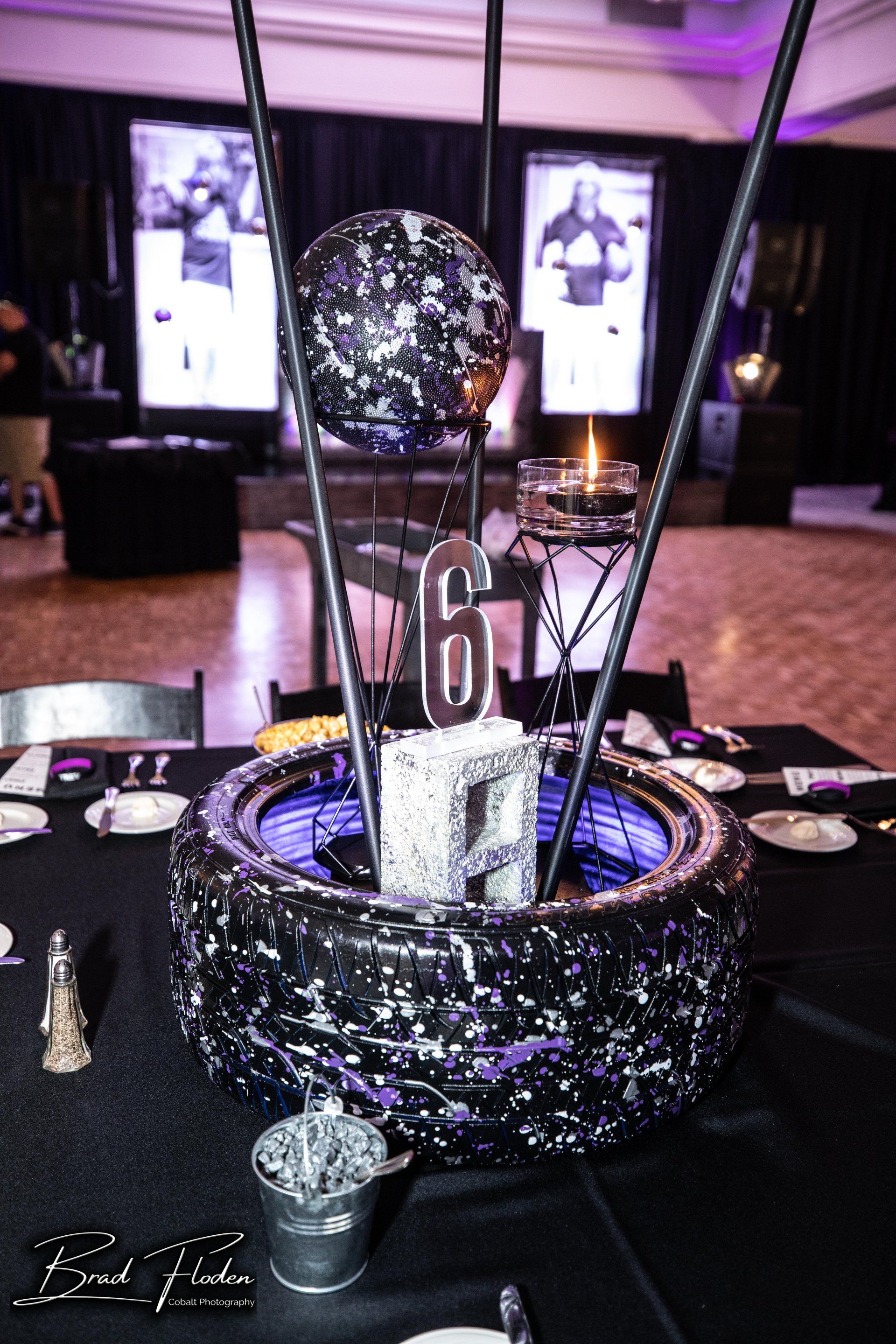 A table with a black table cloth and a black and purple centerpiece with the number 6 on it.