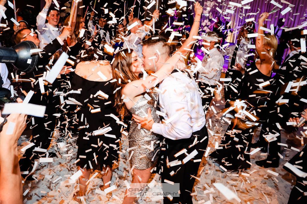 A group of people are dancing in a room with confetti falling from the ceiling.