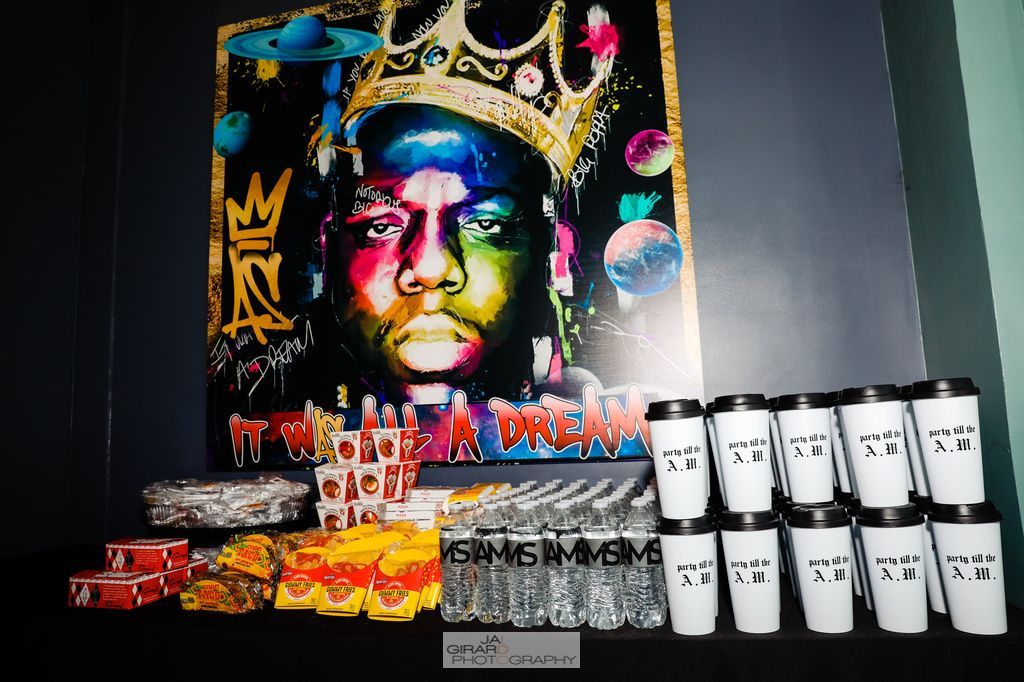 A painting of a man with a crown on his head is on a wall next to a stack of coffee cups.