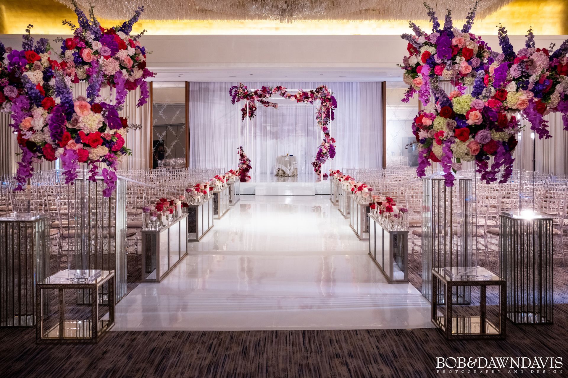 A wedding ceremony is being held in a large room with purple and red flowers.