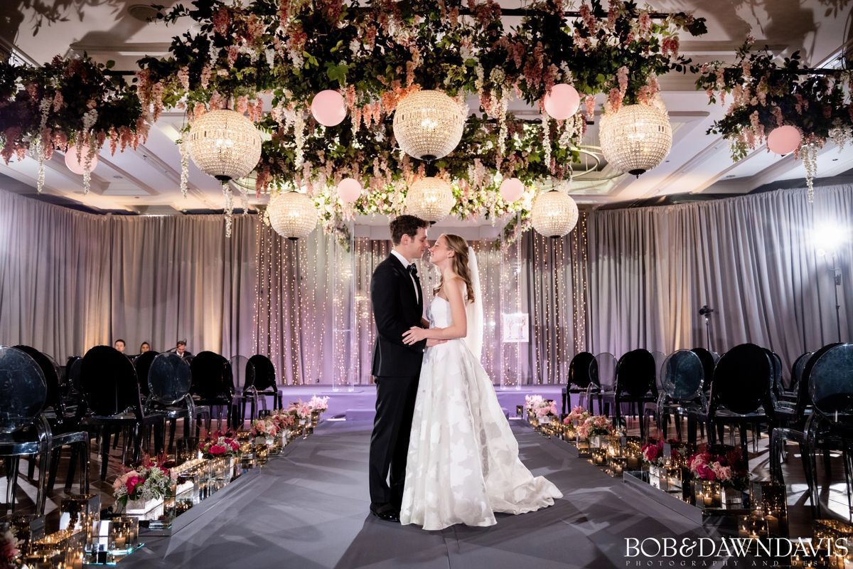 A bride and groom are kissing on the aisle of a wedding ceremony.