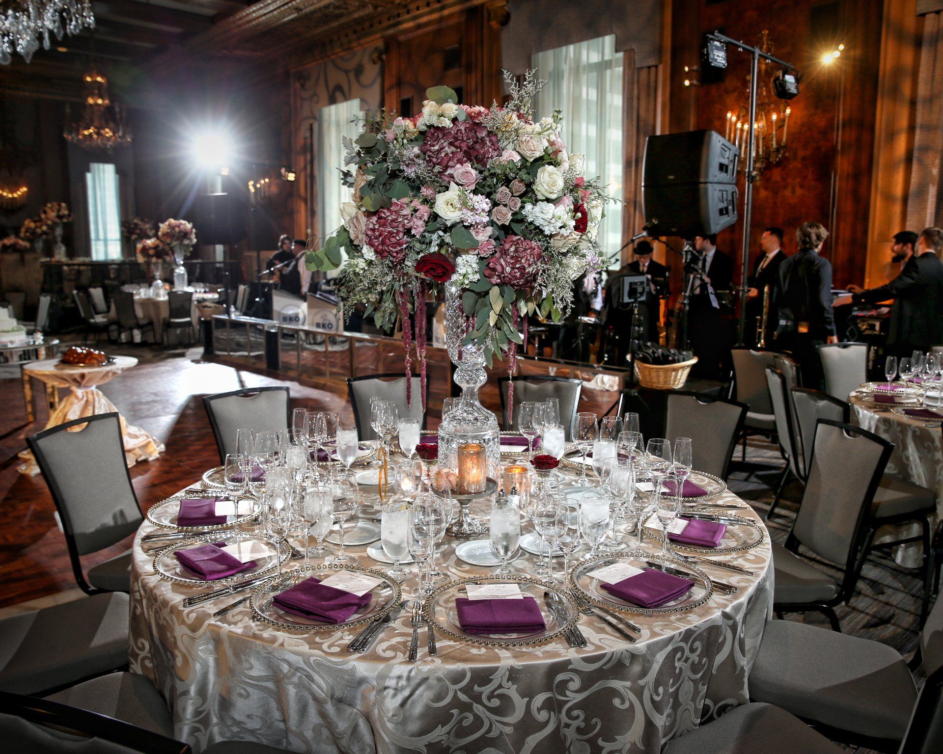 A table set for a wedding reception with a large vase of flowers on it.