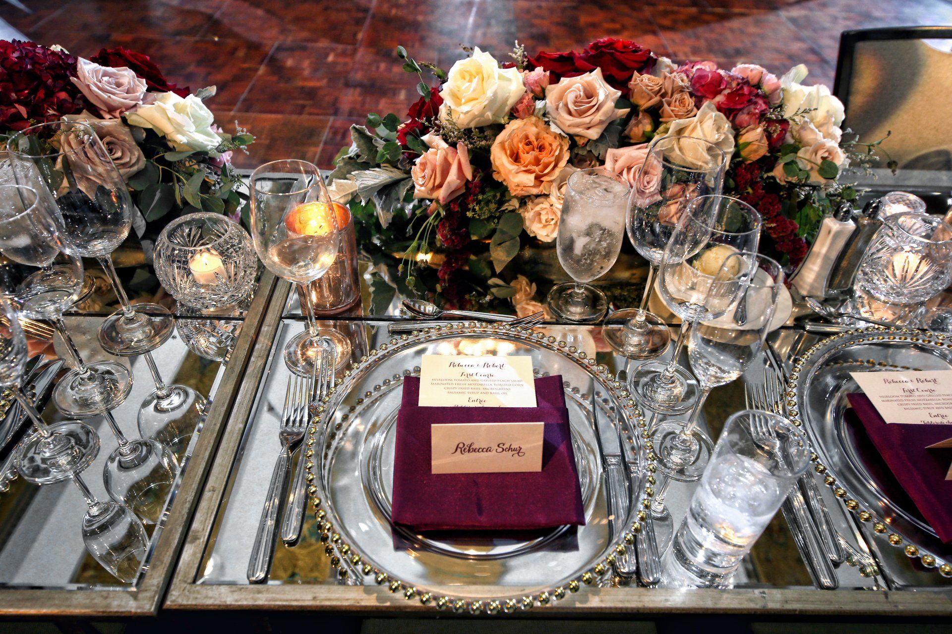 A table set for a wedding reception with plates , glasses , candles and flowers.