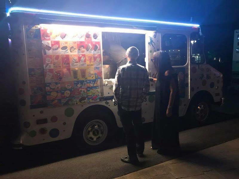 Two people are standing in front of an ice cream truck at night.