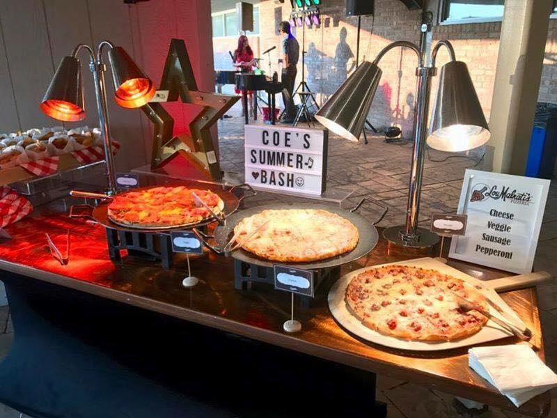 A table with three pizzas on it and a sign that says coe 's summer bash.