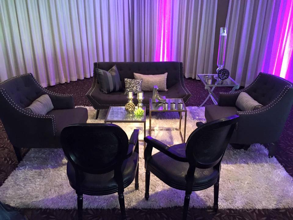 A living room with a couch , chairs , tables and purple lights.