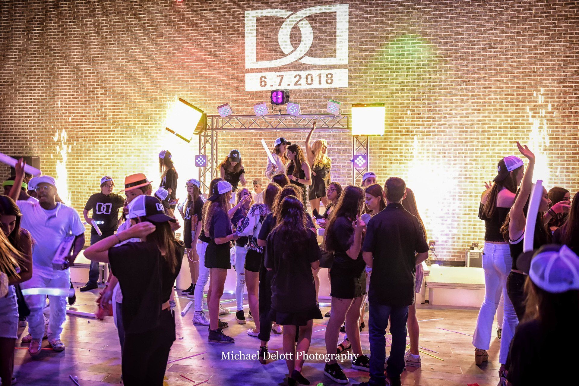 A group of people are dancing in front of a brick wall at a party.