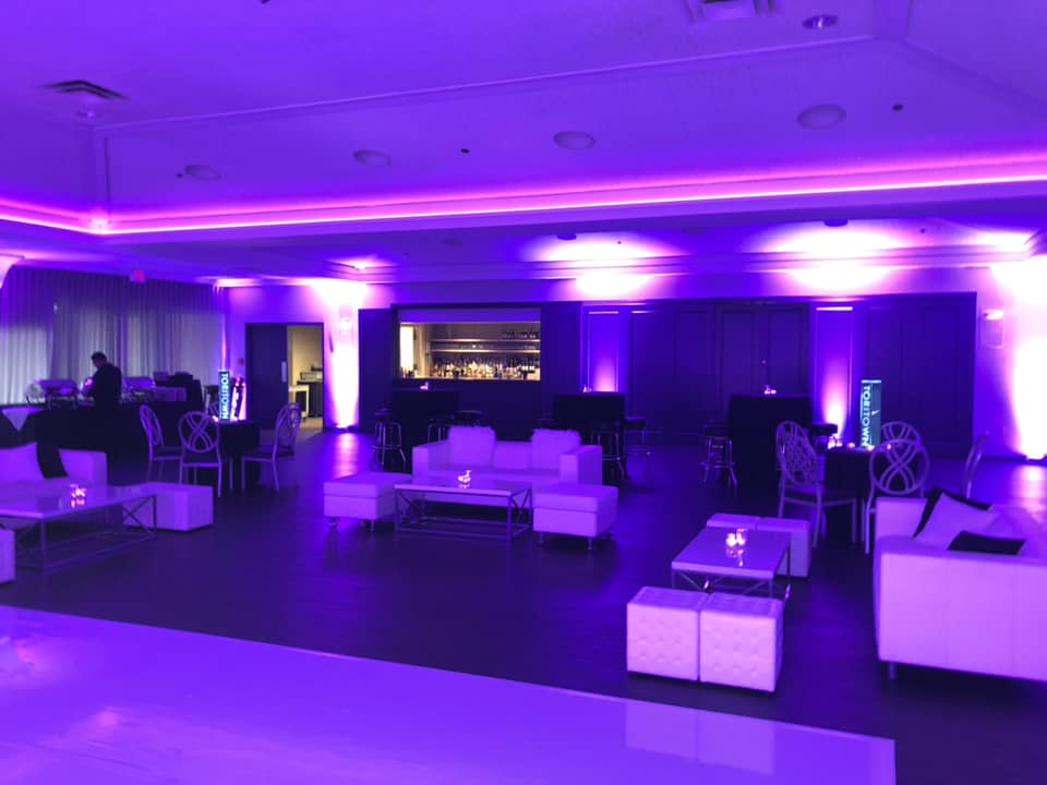 A large room with purple lights and white furniture.
