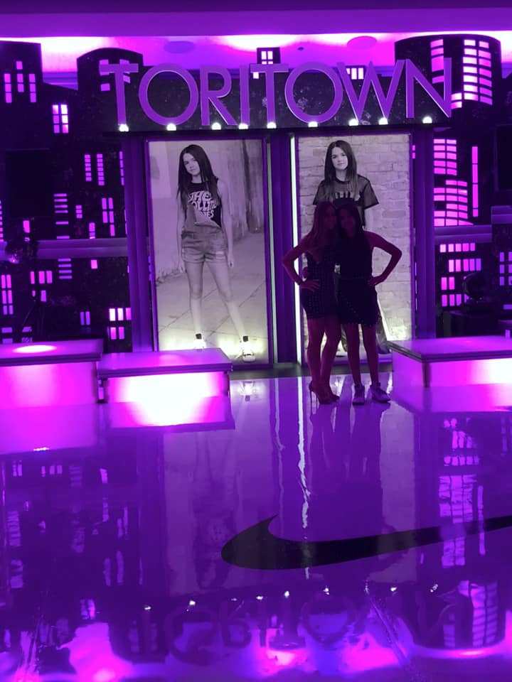 Two girls are standing in front of a sign that says fortown.