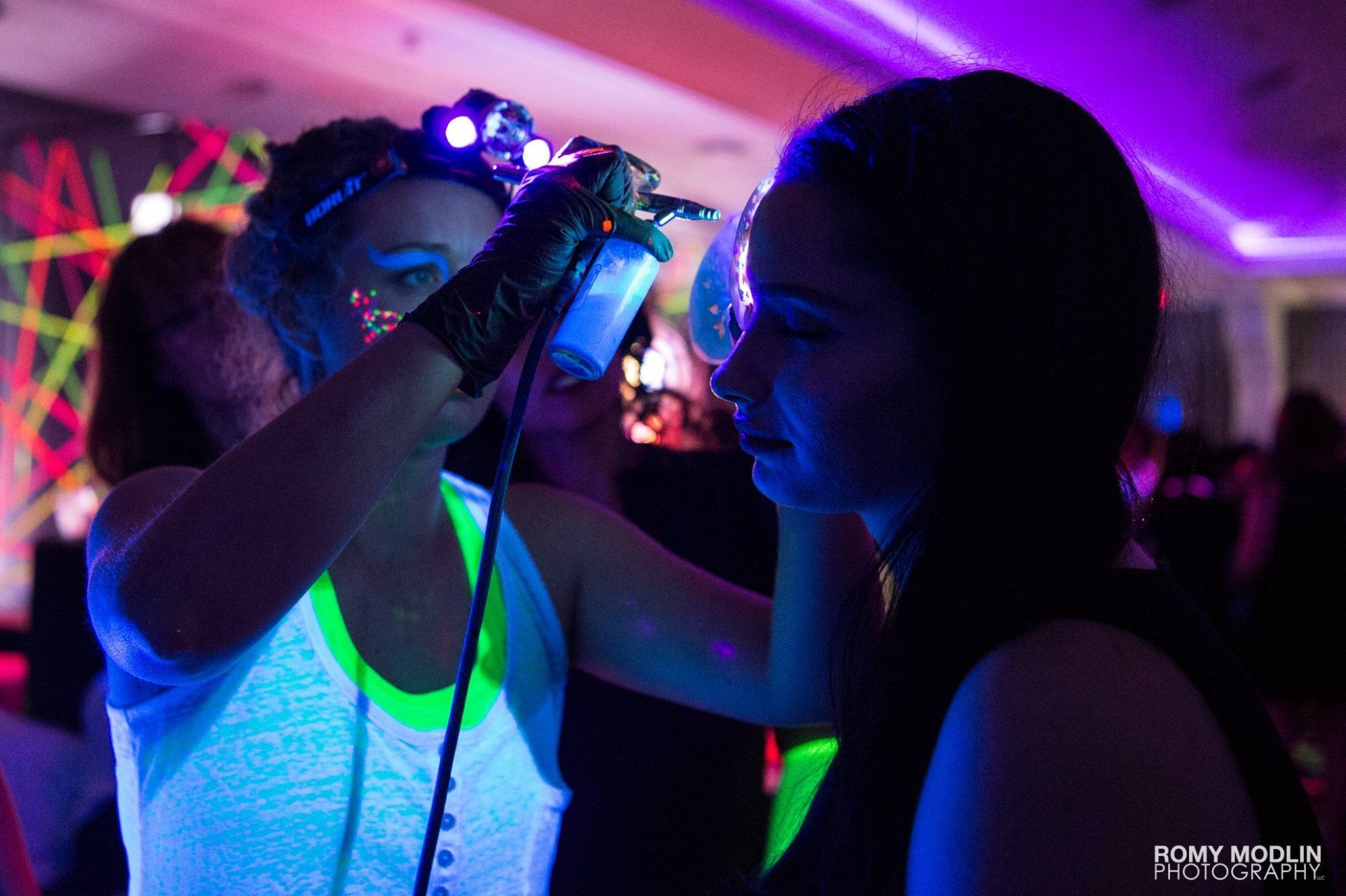 A woman is applying glow in the dark makeup to another woman 's face.