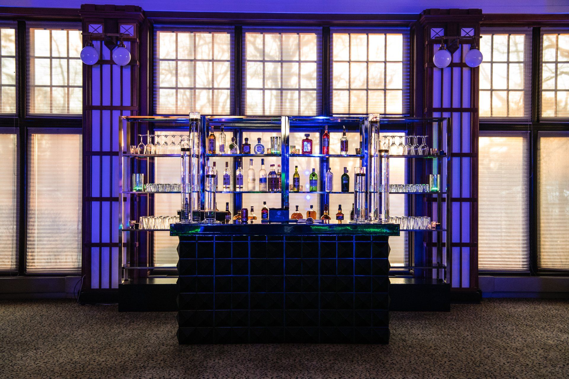 A bar in a room with lots of windows and bottles on shelves