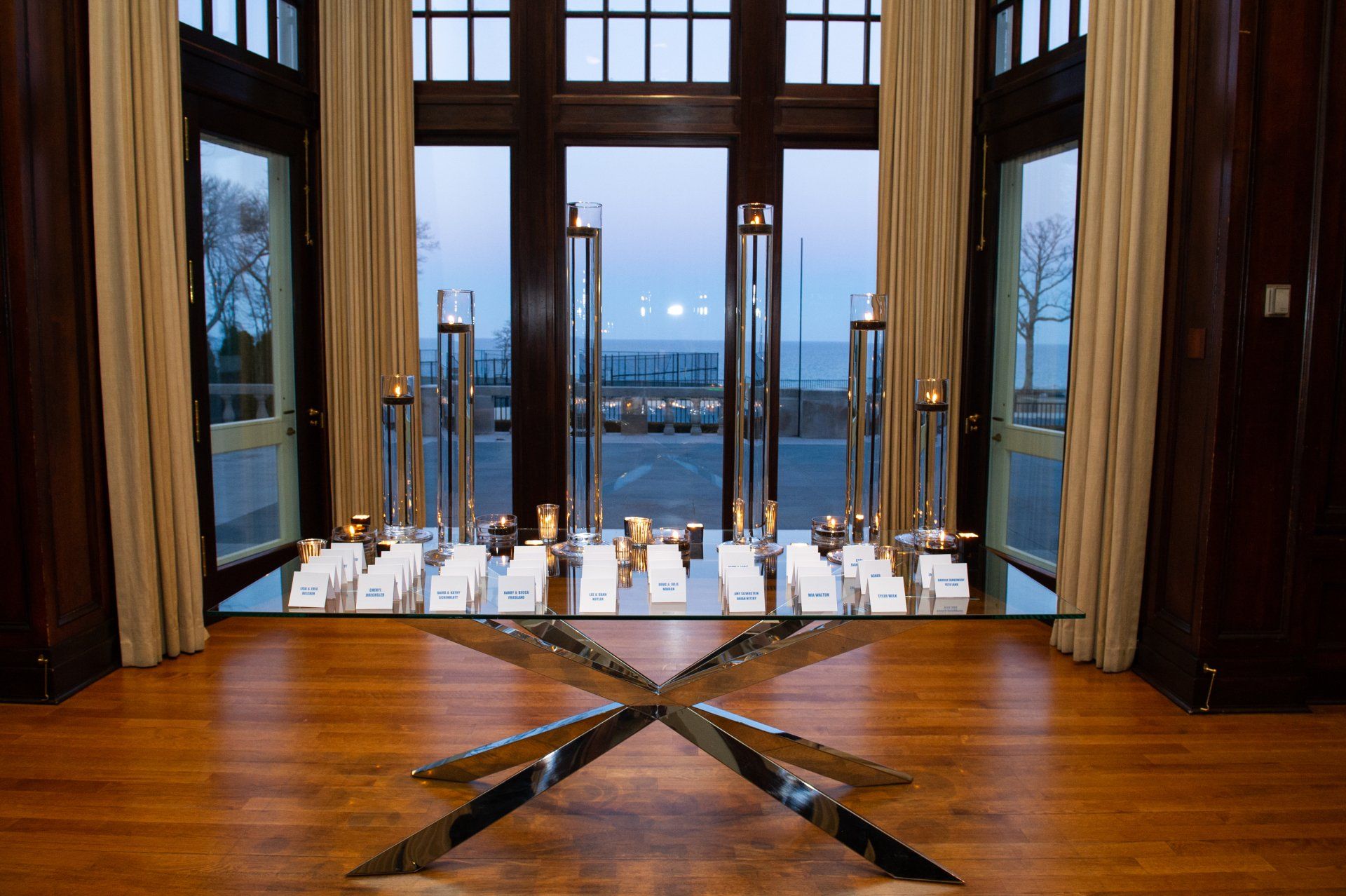 A glass table with candles on it in a room with a view of the ocean.