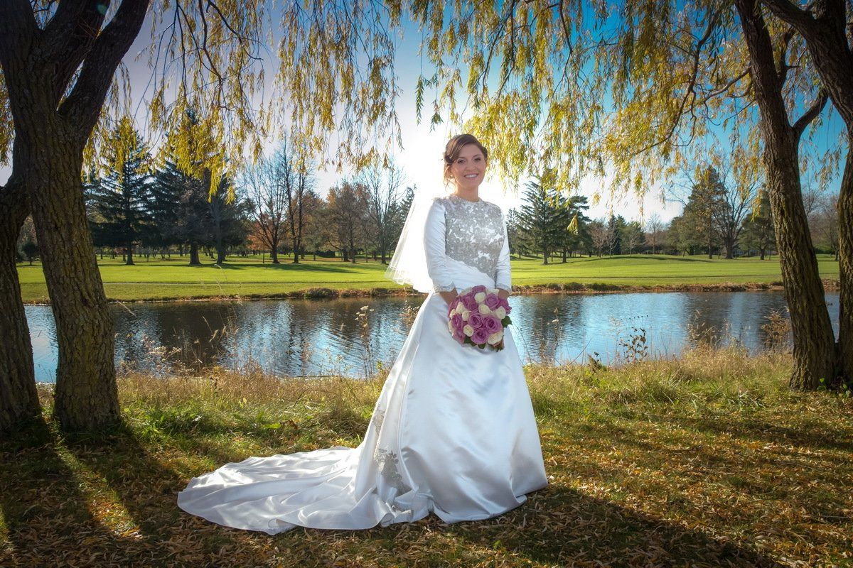 A bride in a wedding dress is standing in front of a lake holding a bouquet of flowers.