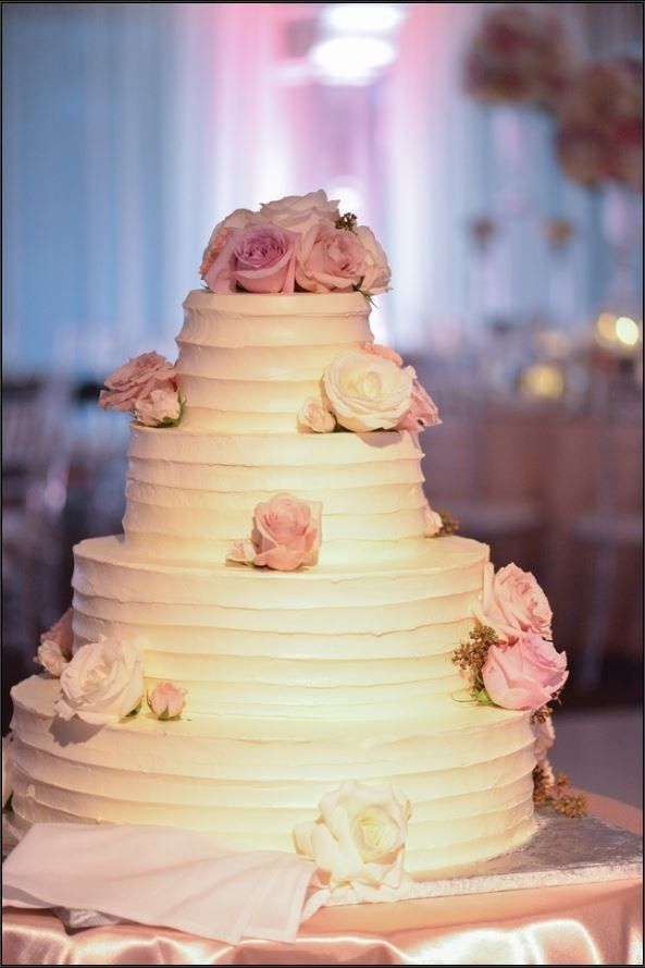 A white wedding cake with pink roses on top