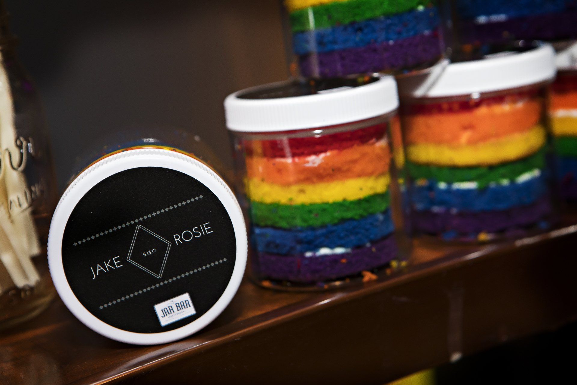 A jar of rainbow colored cake sits on a wooden shelf.