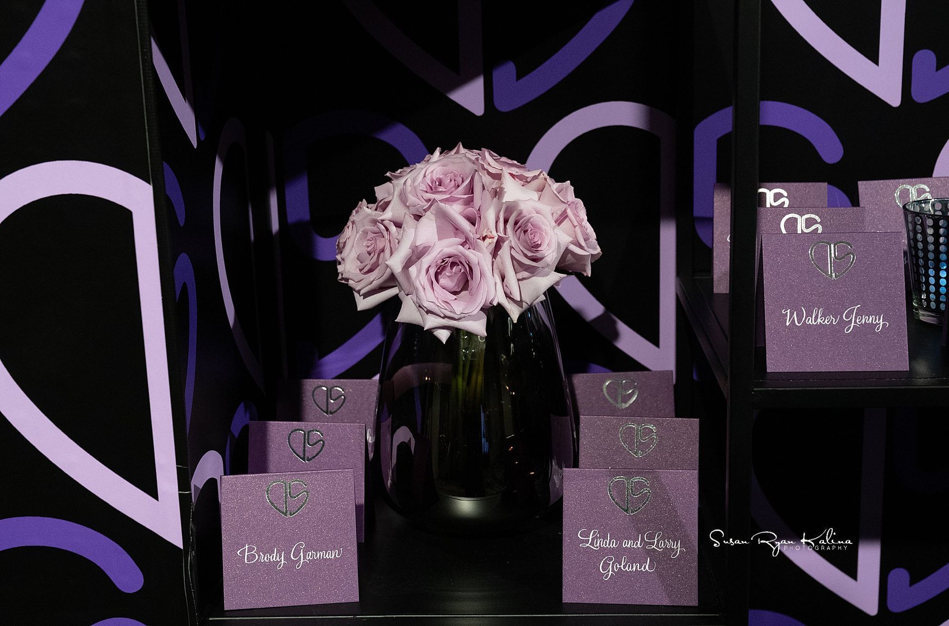 A vase of purple roses sits on a shelf next to purple boxes.