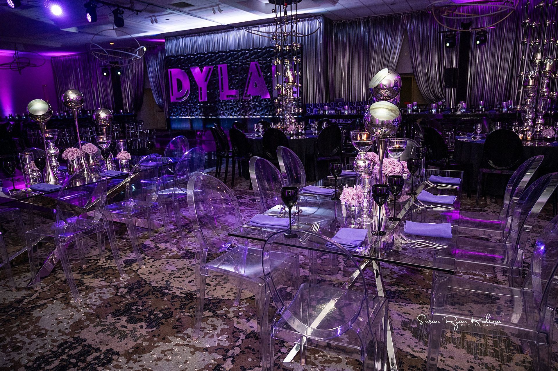 A room with tables and chairs set up for a party with purple lights.