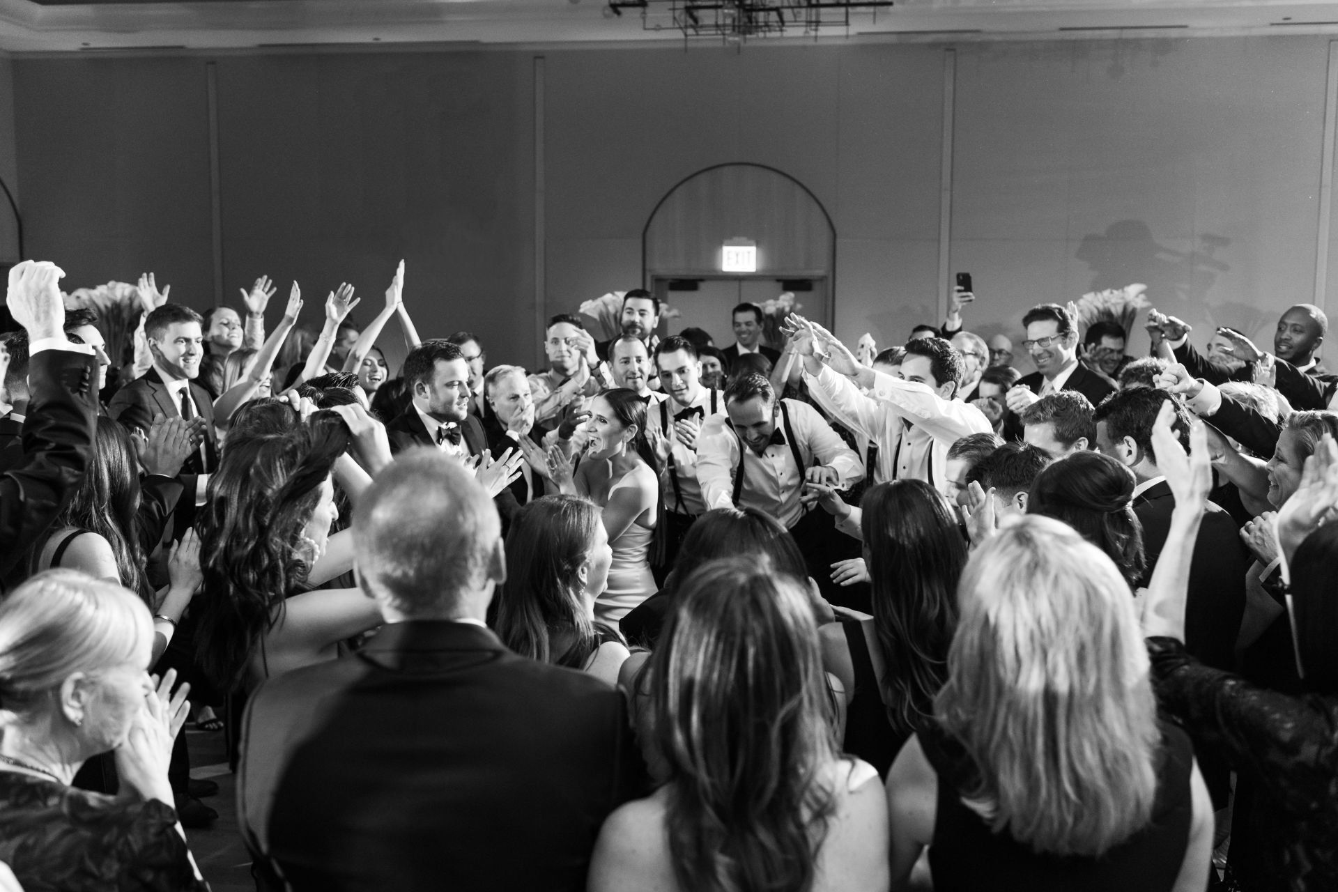 A black and white photo of a crowd of people dancing at a wedding reception.