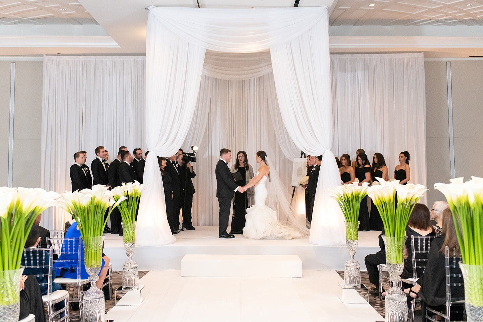 A bride and groom are holding hands during their wedding ceremony under a white canopy.