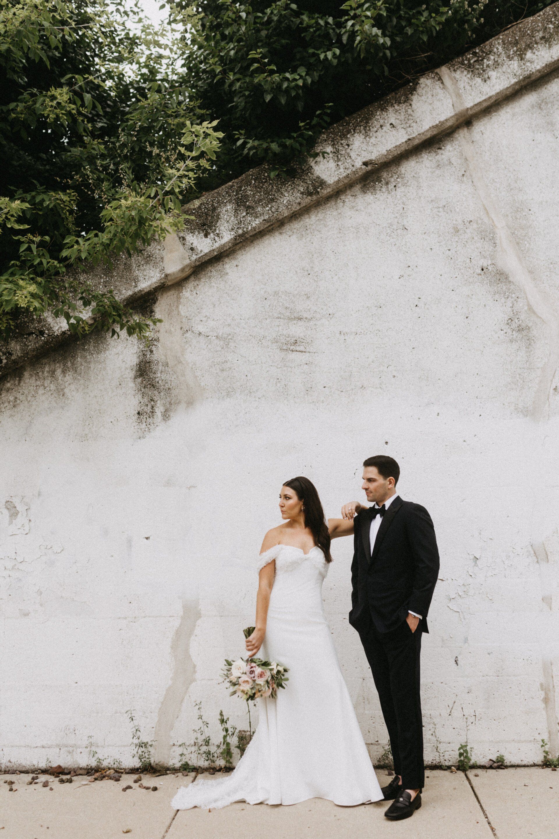 A bride and groom are posing for a picture in front of a white wall.
